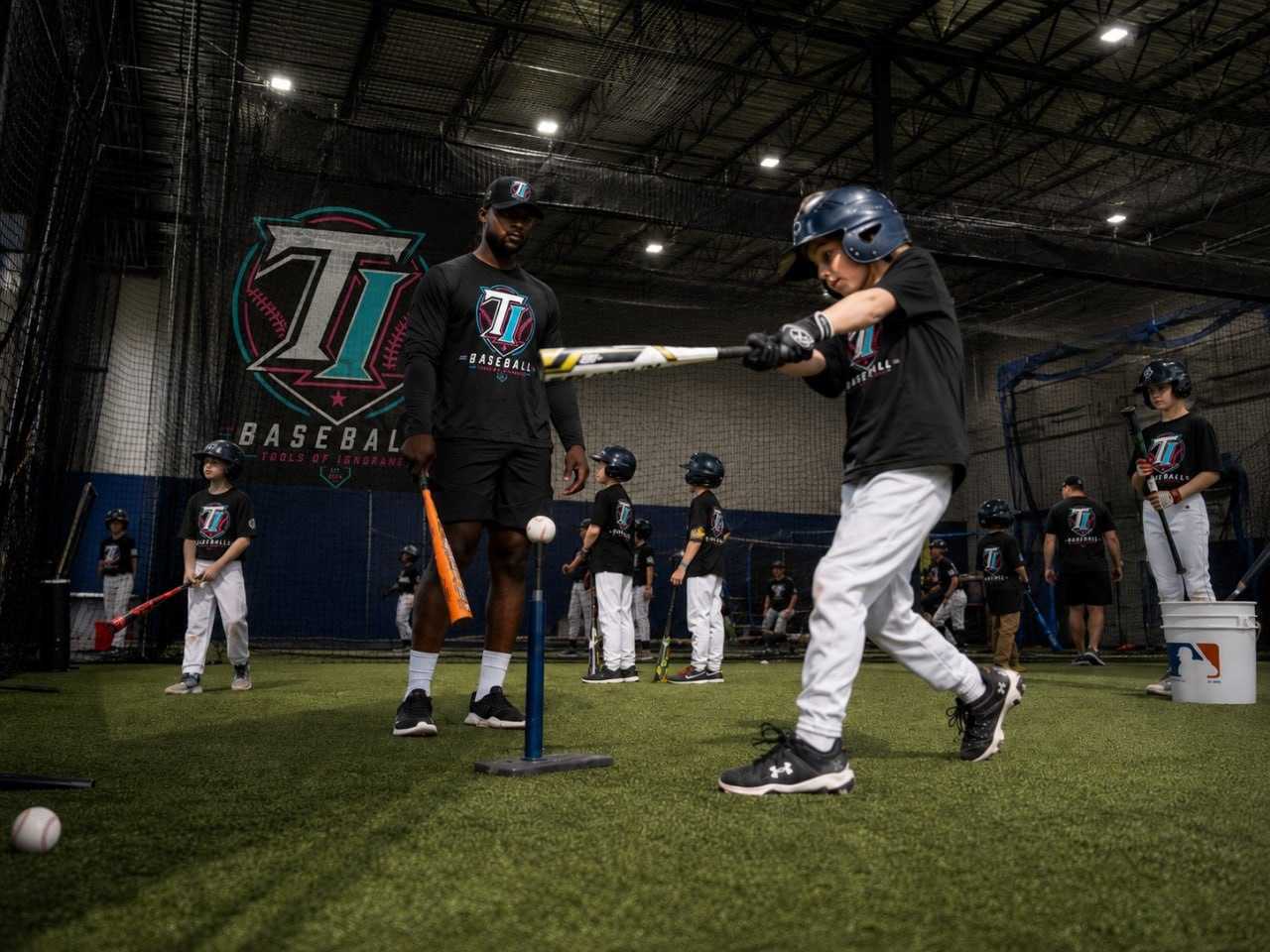 Coach working with a group of young TI Baseball players on tee work at B360 indoor turf